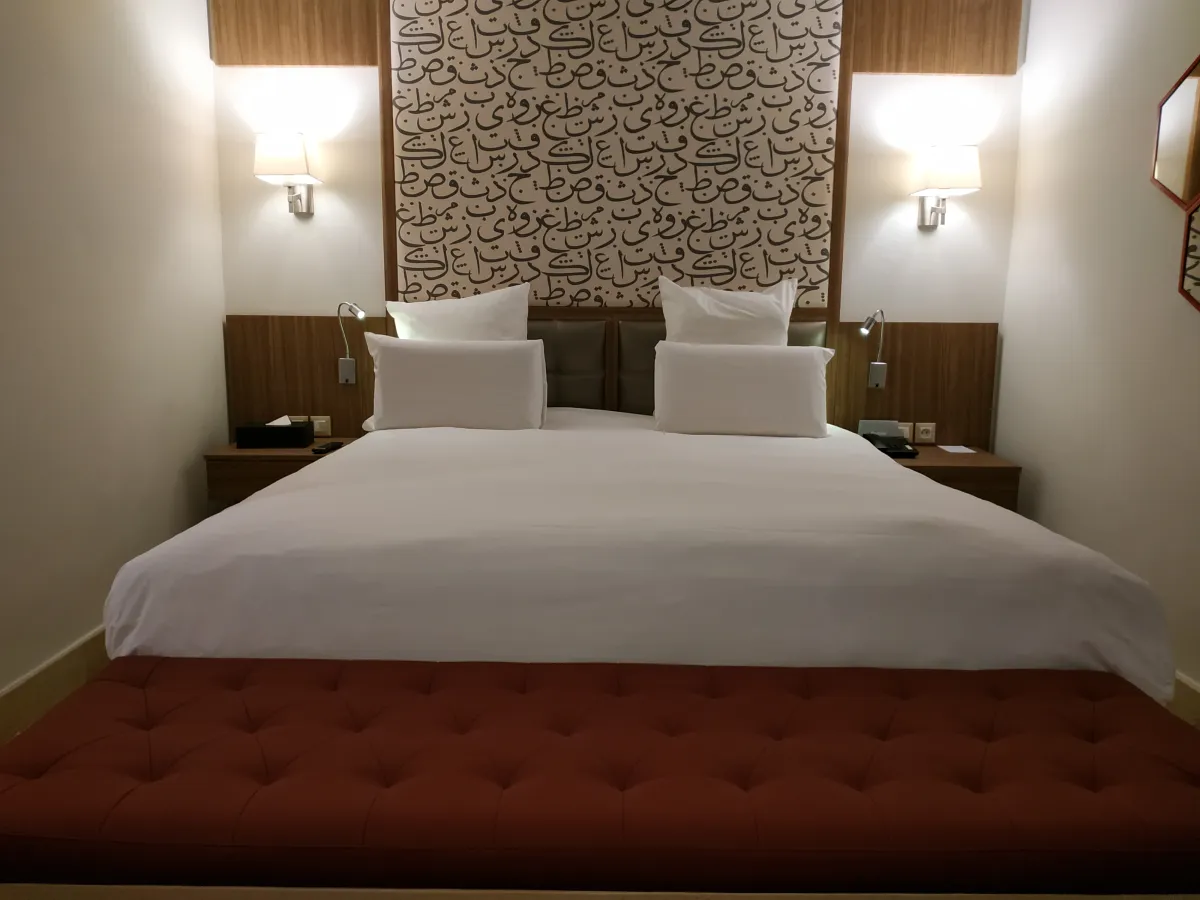 Cama con banco granate y cabecero de caligrafía en el Barceló Marrakech