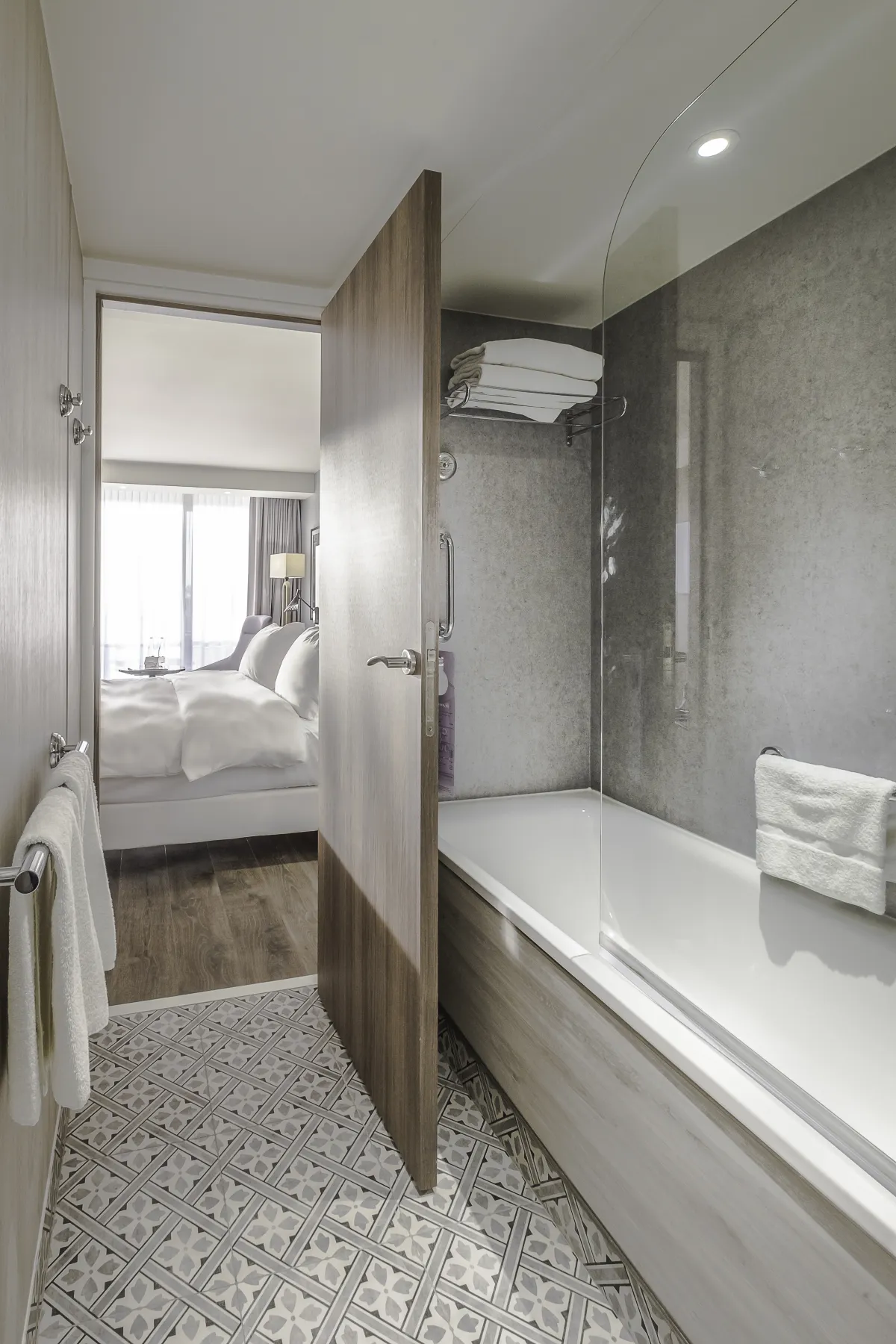 Baño del Radisson Blu Niza con bañera y mampara, con el dormitorio al fondo