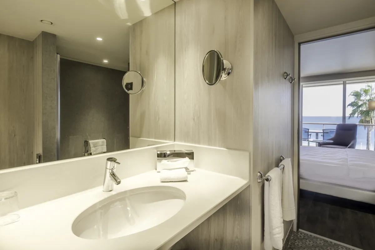 Lavabo curvo y paredes de madera clara en una habitación del Radisson Blu Niza, con el mar al fondo